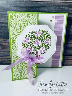 a card with a tree on it and purple ribbon around the bottom corner, in front of a wooden background