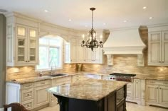 a large kitchen with white cabinets and marble counter tops, chandelier over the island