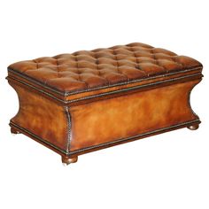 a large brown leather ottoman with studding on the legs and foot rests in front of a white background