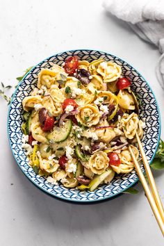 a blue and white bowl filled with pasta salad next to two chopsticks on the side