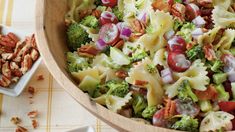 a wooden bowl filled with pasta salad next to two bowls of nuts and other food