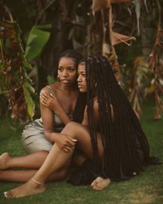 two women are sitting on the grass and one is hugging another woman's chest