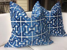 two blue and white pillows sitting on top of a white couch next to each other