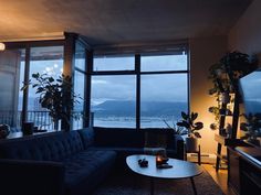 a living room filled with furniture and a large window overlooking the water at night time