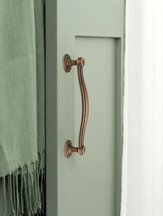 a door handle on the side of a green cabinet with white curtains in the background