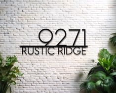 a sign that reads 927 rustic ridge on a brick wall next to potted plants