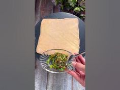 a person holding a spoon over a bowl filled with food on top of a wooden table