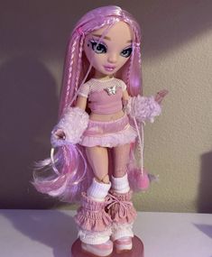 a doll with pink hair and white socks holding a teddy bear in her hand while standing on top of a table