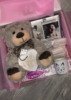 a teddy bear sitting in a pink box with other items around it and a coffee mug