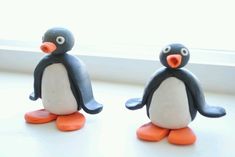 two small plastic penguins sitting on top of a window sill next to each other