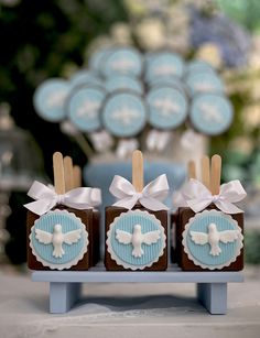 three chocolates with white bows on them are sitting on a blue stand in front of some cupcakes