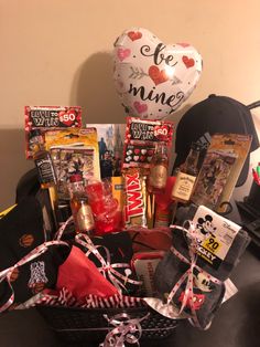 a basket filled with lots of different items on top of a table next to a heart shaped balloon