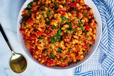 a white bowl filled with pasta and meat on top of a blue towel next to a spoon