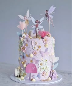 a pink cake decorated with fairy figurines and flowers