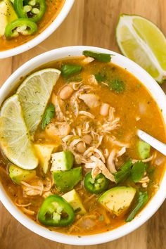 a white bowl filled with chicken chili soup and topped with avocado, limes and sliced jalapenos