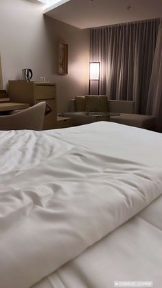 a bed with white sheets and pillows in a bedroom next to a couch, table and chair