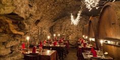 a dimly lit dining area in an old wine cellar with red tablecloths and lights hanging from the ceiling