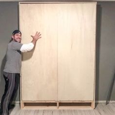 a man standing in front of a large wooden cabinet with his hands out to the side