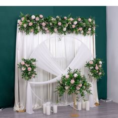 a wedding arch with flowers and greenery on the wall next to white drapes