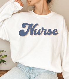 "Nothing looks more stylish and chic than this Retro Registered Nurse Crewneck.  This Sweatshirt comes in multiple color options. This is a perfect gift for yourself or any RN you know! This unisex heavy blend crewneck is made of polyester and cotton to provide a comfortable and cozy feel. The collar is ribbed knit and retains its shape after every wash.  WHAT IT SAYS:  Nurse ITEM DETAILS:  -50% cotton, 50% polyester -Medium-heavy fabric  -Loose fit -Sewn-in label -Runs true to size, BUT if you're looking for a more \"baggy\" fit we suggest sizing up! **Please note that the lettering may be slightly less vibrant or bright on the actual printed sweatshirt. This is due to which color option it's printed on and the printed ink.  LOOKING FOR  THIS SWEATSHIRT IN ANOTHER DESIGN OR STYLE? CLICK O White Long Sleeve Nursing T-shirt, Fall Crew Neck Nursing Top, White Relaxed Fit Sweatshirt For Nursing, Casual Long Sleeve Nursing Tops, Fall Nursing Sweatshirt With Crew Neck, Nursing Long Sleeve Relaxed Fit Sweatshirt, Casual Cotton Sweatshirt For Nursing, Relaxed Fit Nursing Tops With Crew Neck, Long Sleeve Nursing Sweatshirt With Relaxed Fit