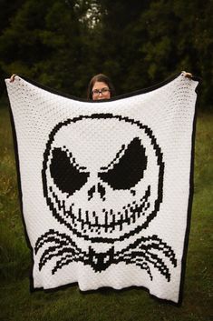 Woman holds up a large crocheted blanket of Jack Skellington. The blanket is in black and white, and features Jack's head with a smirk on his face and signature bat bow tie. The woman is standing in front of a dark, ominous looking cluster of trees. Nightmare Before Christmas Crochet, Daffodil Craft, Bat Bow, C2c Blanket, Crochet Pour Halloween, C2c Crochet Pattern Free, Yarn Weights, Yarn Project, Throw Blanket Pattern