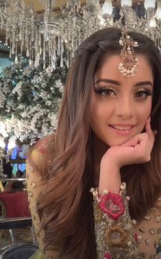 a woman with long brown hair wearing a head piece and jewelry in front of a chandelier