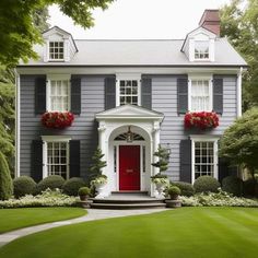 a large gray house with red door and window boxes on the front porch, surrounded by lush green grass