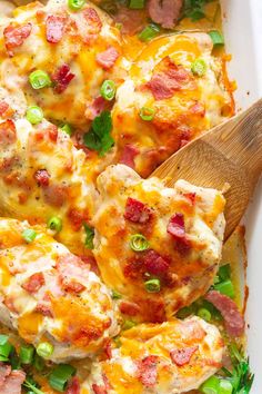 a casserole dish with meat, cheese and green onions in it next to a wooden spoon