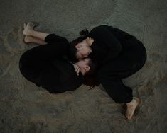 a woman laying on the sand with her head in her hands and eyes closed,