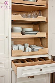 an open cabinet with dishes and glasses in the bottom drawer, next to a white cupboard