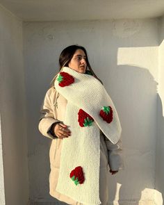 a woman wearing a knitted scarf with strawberries on it, standing in front of a white wall