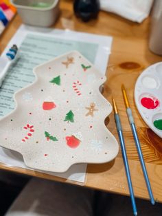 a plate with christmas decorations on it next to paintbrushes and watercolors