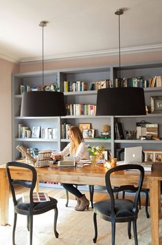 a woman sitting at a wooden table in front of a book shelf filled with books