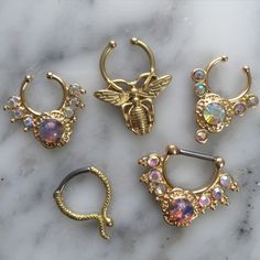 four pairs of gold colored opal nose rings on a marble surface with a bee