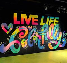 a large mural on the side of a building that says, live life happily written in multicolored letters