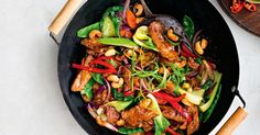 a wok filled with meat and vegetables on top of a table