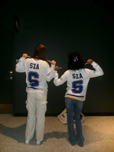 two women in white jerseys standing next to each other with their hands behind their backs