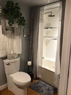 a white toilet sitting next to a bath tub in a bathroom under a window with curtains