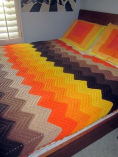 a bed with a colorful blanket on top of it next to two pillows and a window