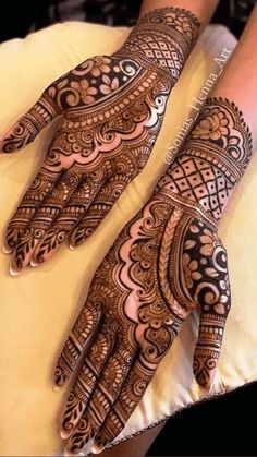 two hands with henna designs on them sitting on a cushion in front of a woman's arm