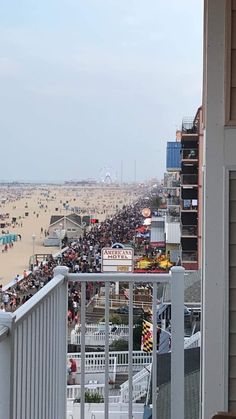 a crowded beach with people on the sand and in the water, from a balcony