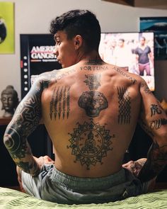 a man with tattoos sitting on top of a bed