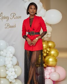 a woman standing in front of balloons wearing a red jacket and black mesh skirt with high heels