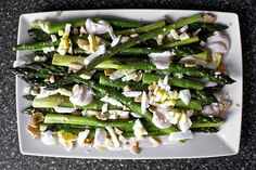 asparagus with garlic, almonds and dressing on a white square plate sitting on a black table