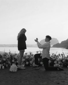 a man kneeling down next to a woman in front of flowers and candles on the beach