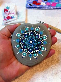 a hand holding a painted rock in the shape of a snowflake with beads on it