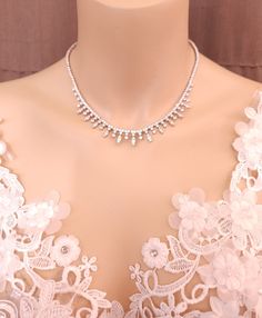 a close up of a dress with white lace and pearls on the neck, as well as a necklace