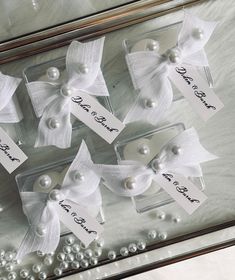 white bows and pearls are on display in a glass case with name tags attached to them