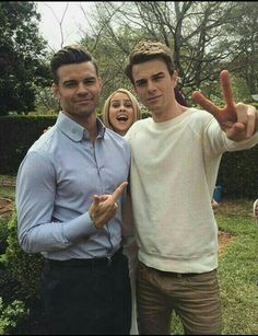 two men standing next to each other giving the peace sign with their fingers in front of them