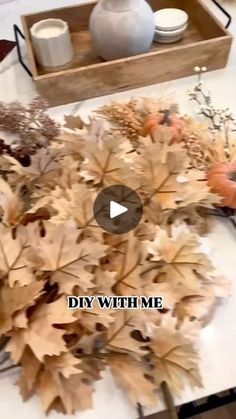 someone is arranging fake leaves on a table with a vase and other items in the background